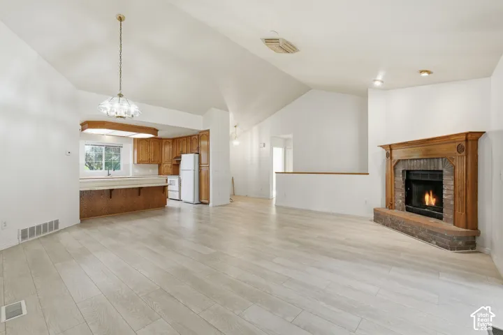 Living and dining area fully vaulted ceilings, wood-finish flooring, brick-surround fireplace with a wood mantel, and kitchen cabinetry with integrated lighting