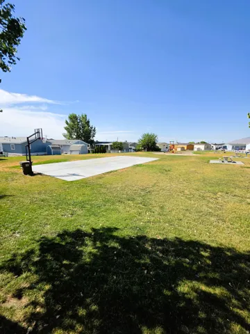 Expansive green space featuring a concrete sports court and a basketball hoop