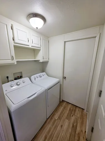 Dedicated laundry area featuring white cabinetry with ample storage, a built-in shelf, and wood-finish flooring