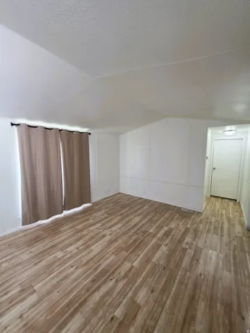 Expansive interior space featuring wood-finish flooring, light-toned walls, and a window with curtain rod