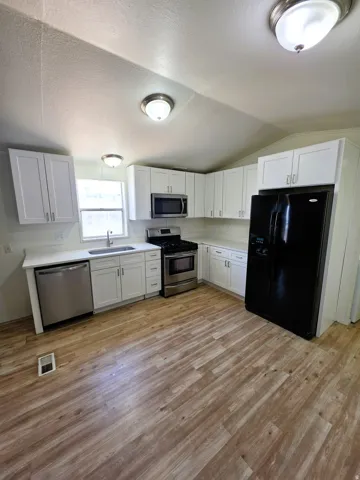 Kitchen featuring wood-finish flooring, white cabinetry, white quartz countertops, a stainless steel dishwasher, and a stainless steel range with an overhead microwave