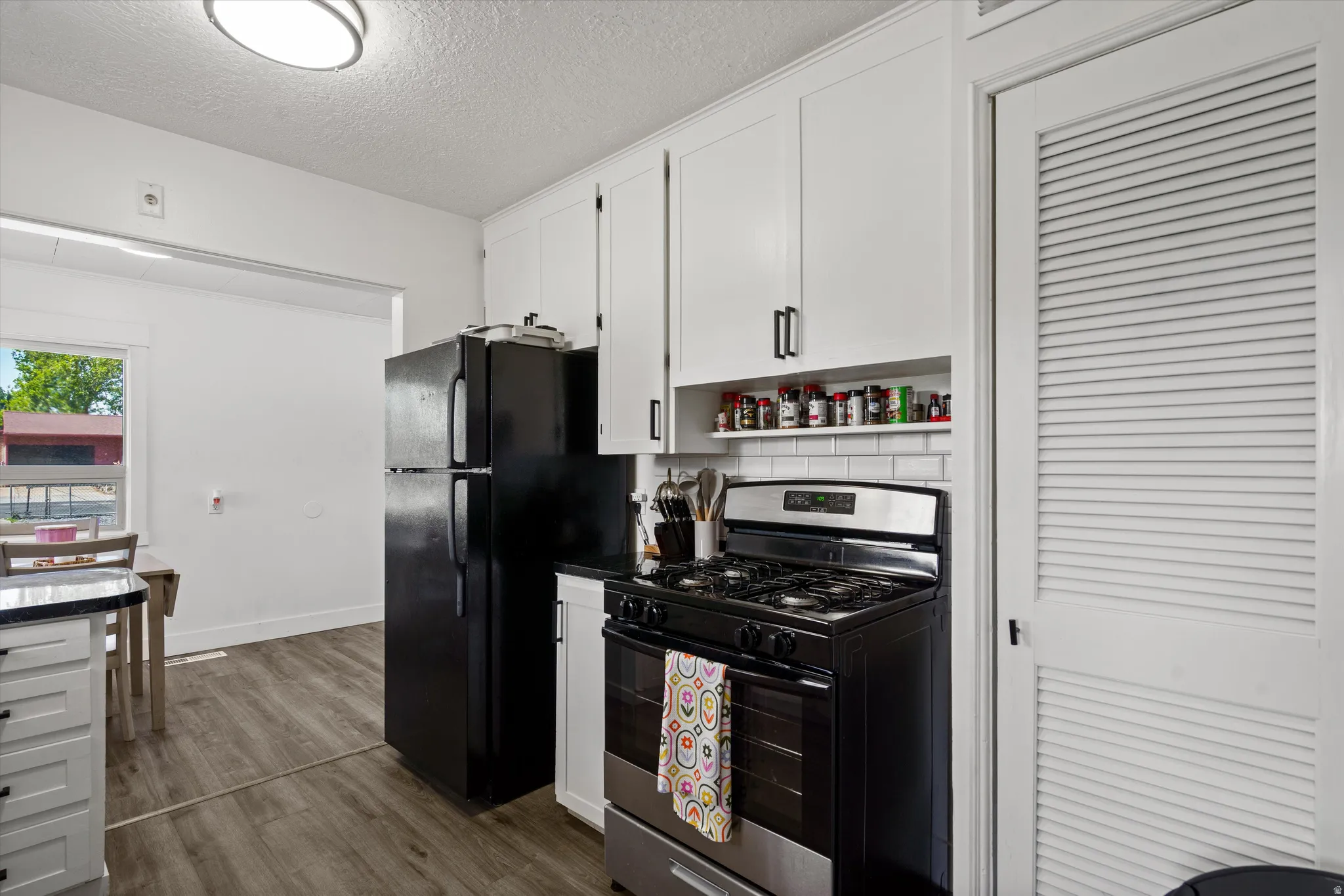 Kitchen featuring white shaker-style cabinetry with matte black hardware, stainless steel and black gas range, white subway tile backsplash, and a built-in spice rack