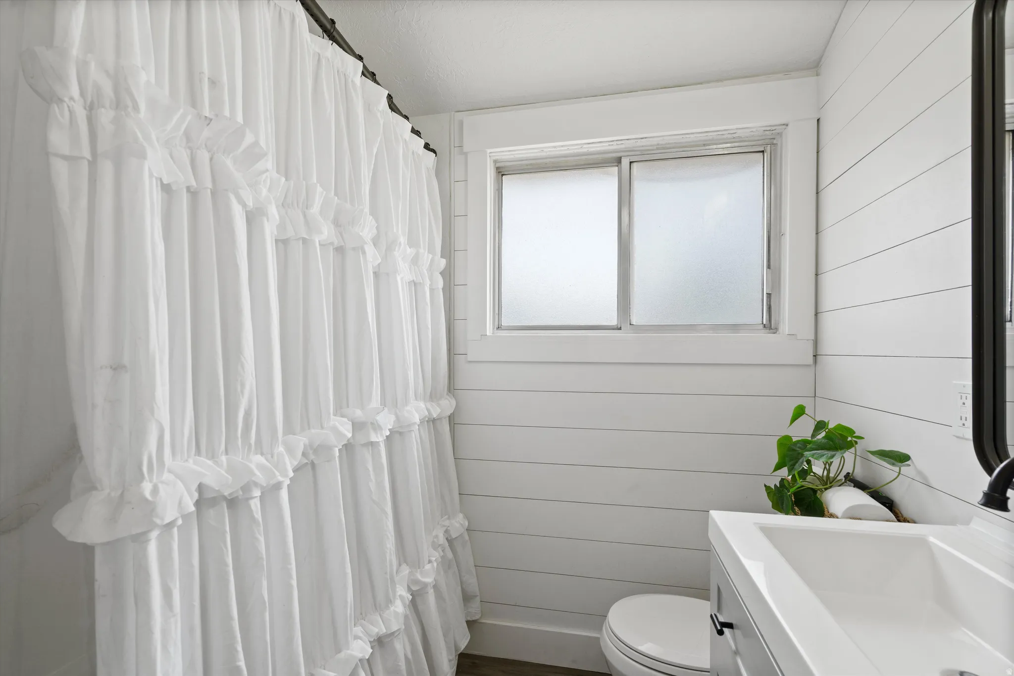 Bathroom featuring shiplap walls, a frosted window, and a vanity with an integrated sink and matte black hardware