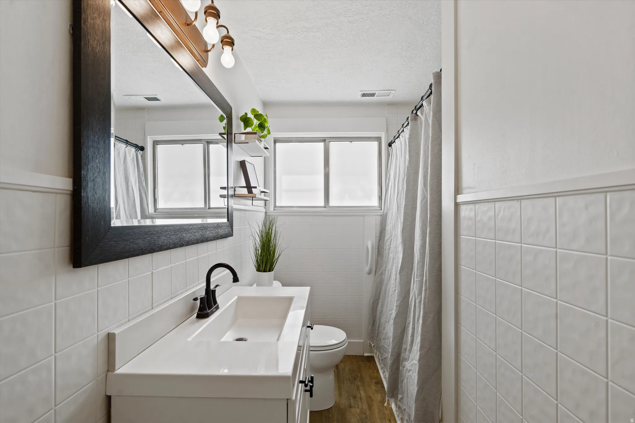 Bathroom featuring a single vanity with a white countertop and integrated sink, a large framed mirror, matte black faucet, and a wall-mounted light fixture with three exposed bulbs