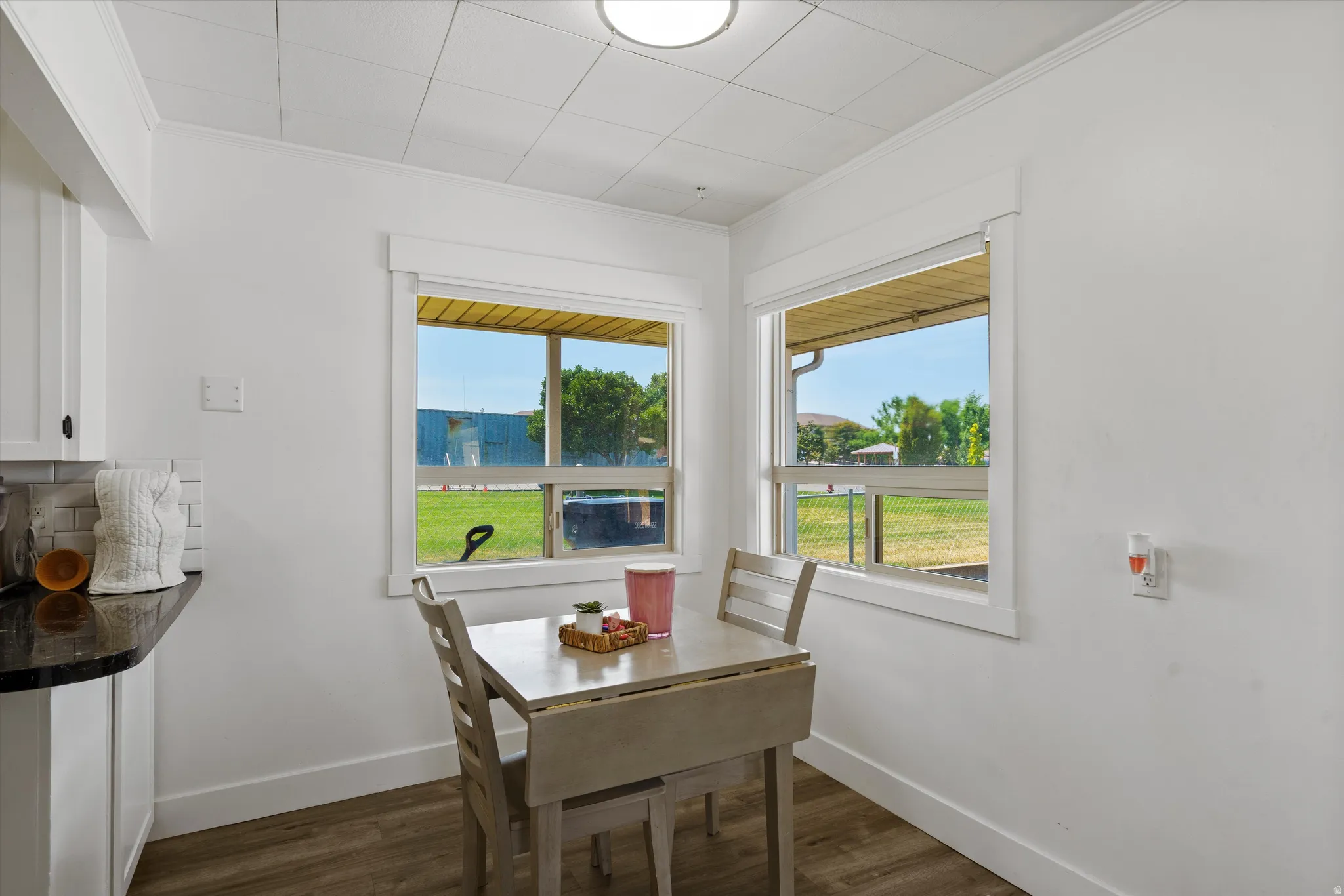 Dining area featuring two windows, wood-finish flooring, white trim, and a drop-leaf table