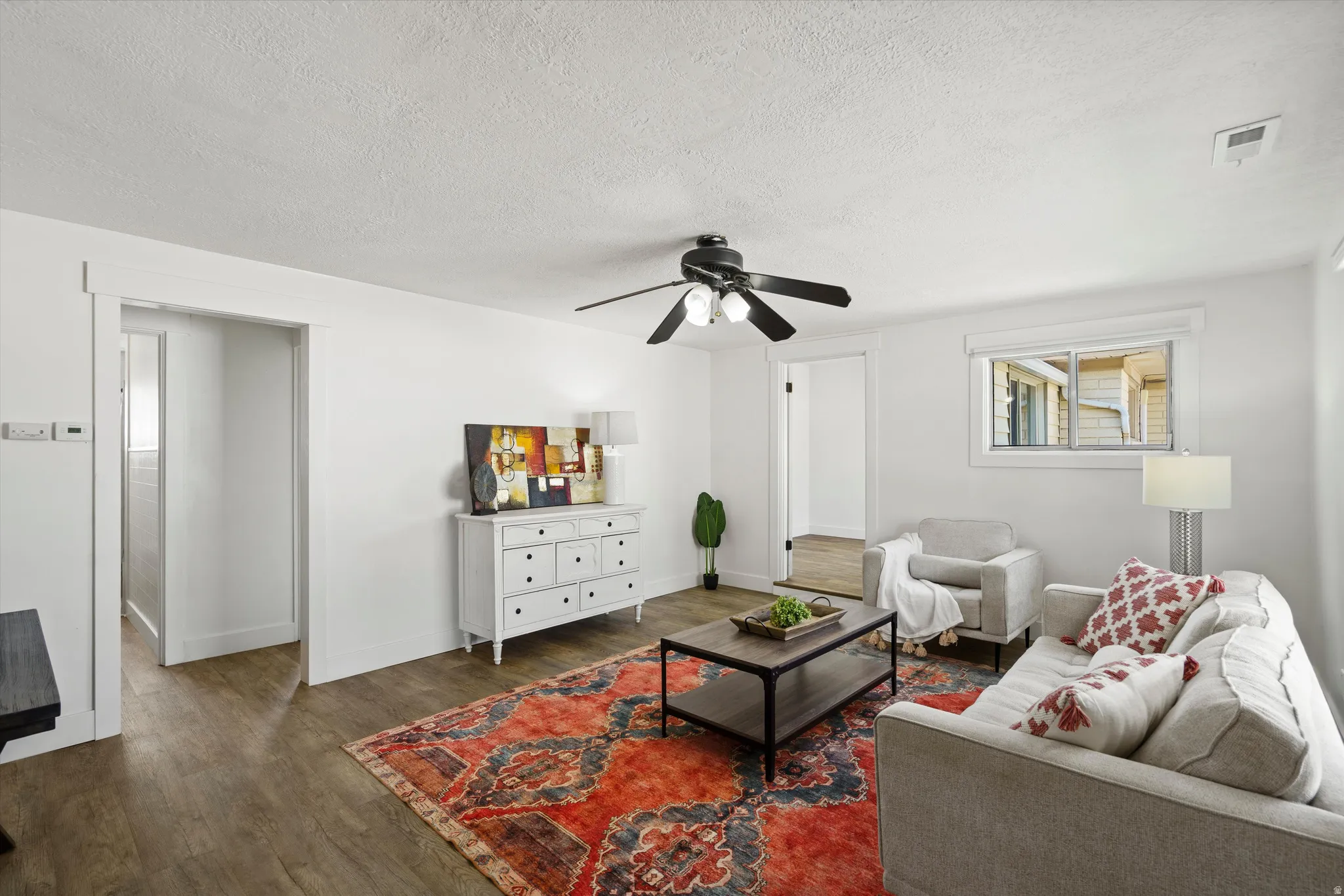 Living area featuring wood-finish flooring, white walls, a ceiling fan with integrated lighting, and a window with white trim