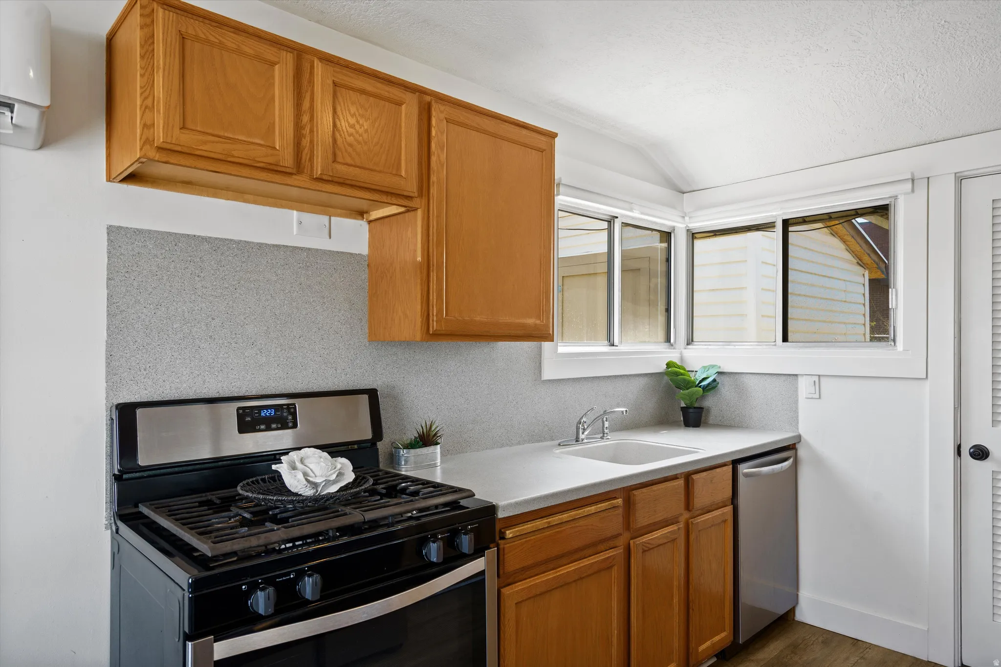 Kitchen featuring wood cabinetry, light-toned countertops, stainless steel appliances, and a grey speckled backsplash