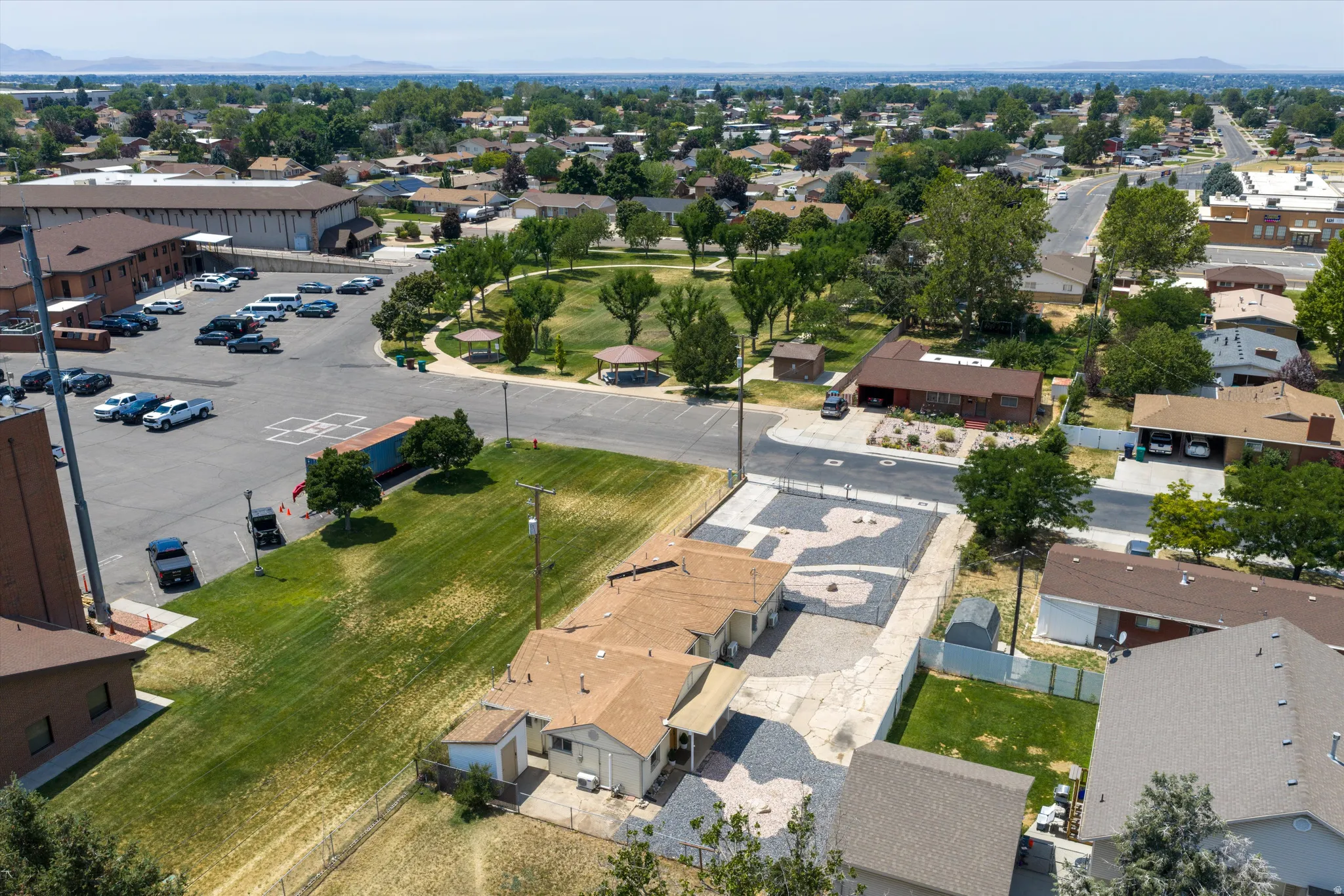 Aerial perspective showcasing multiple properties with brown shingle roofs, adjacent to a large paved parking area and a green park space