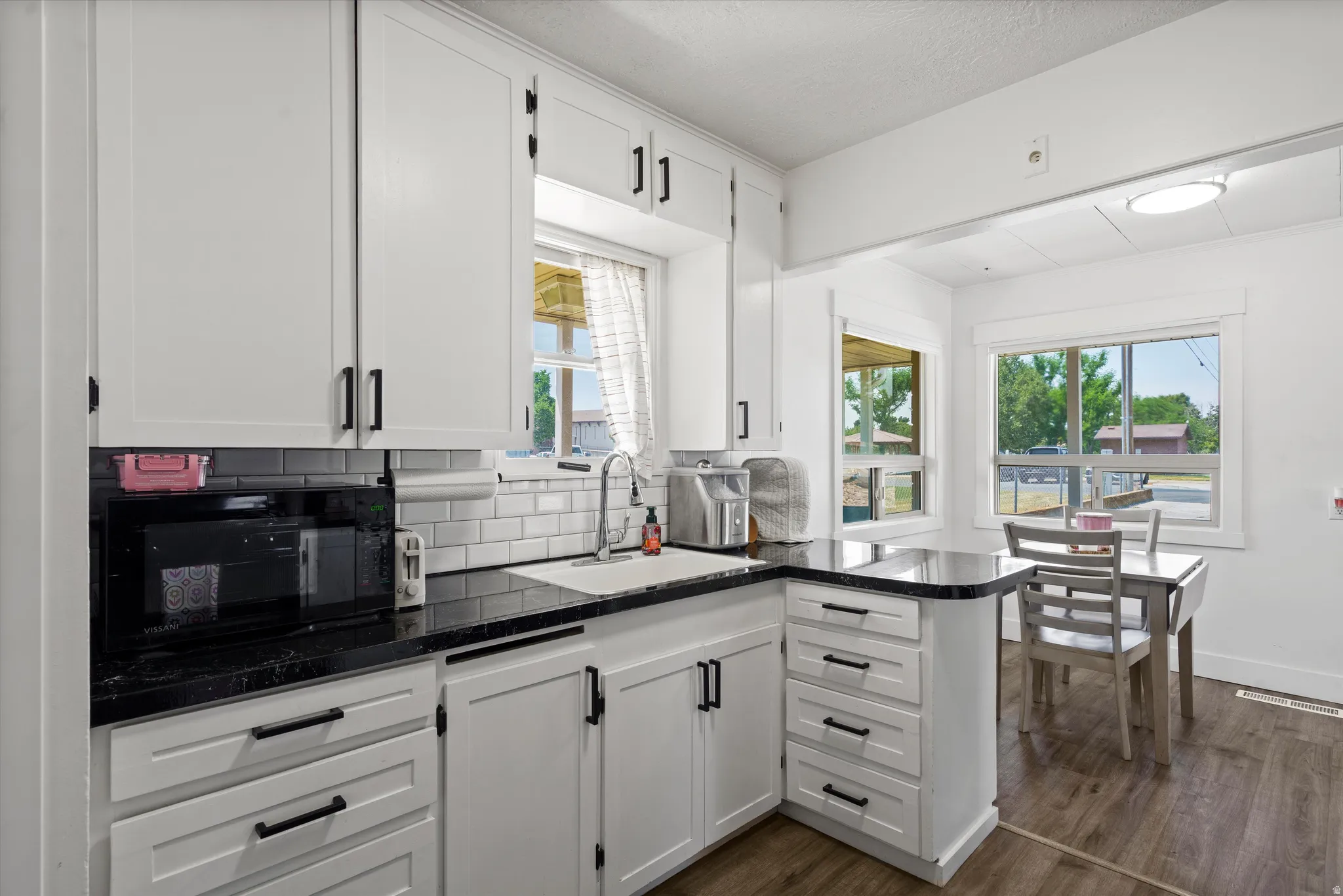 Kitchen featuring white shaker-style cabinetry with matte black hardware, dark stone countertops, and a white subway tile backsplash