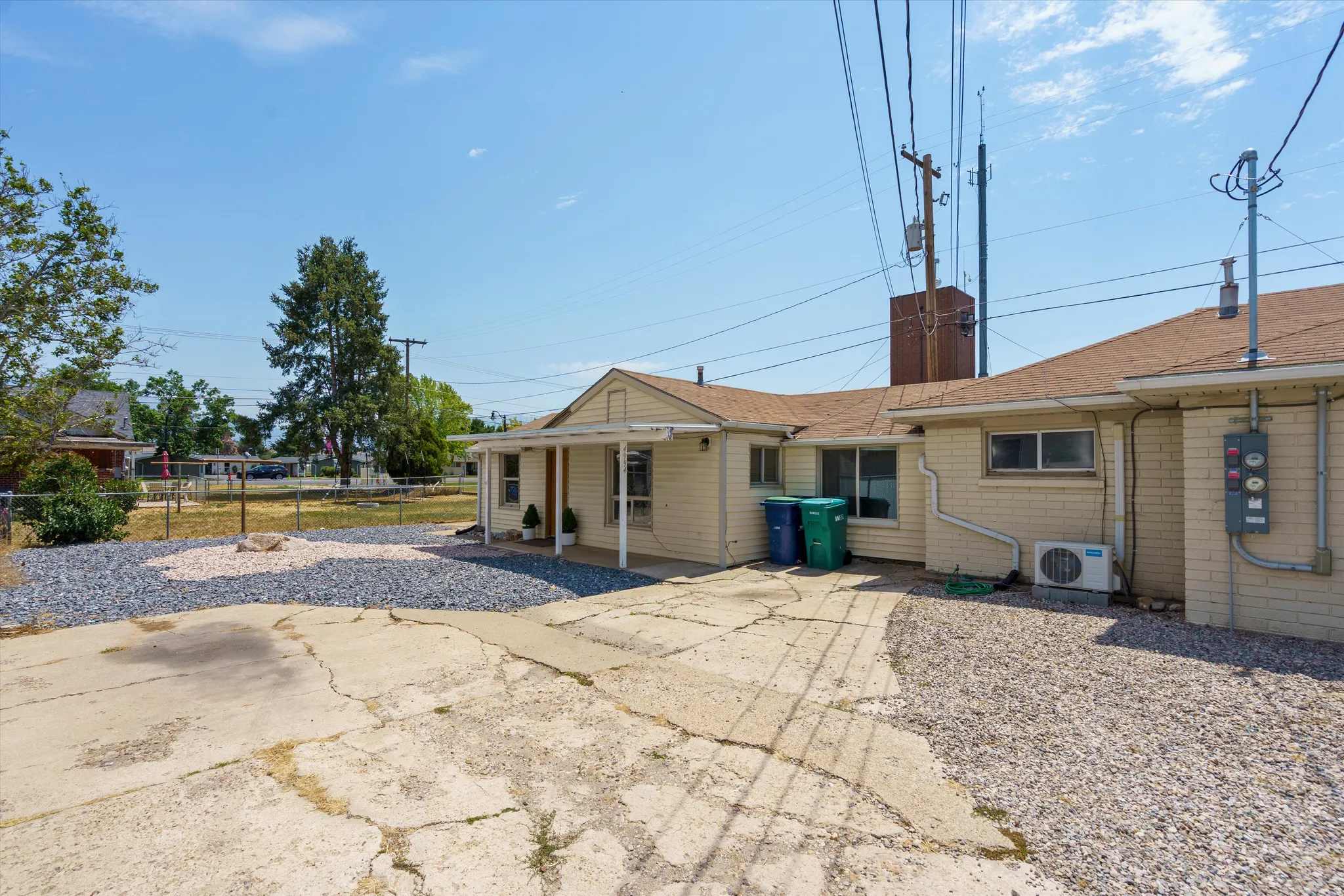 Rear exterior with a concrete patio, gravel landscaping, and mature trees