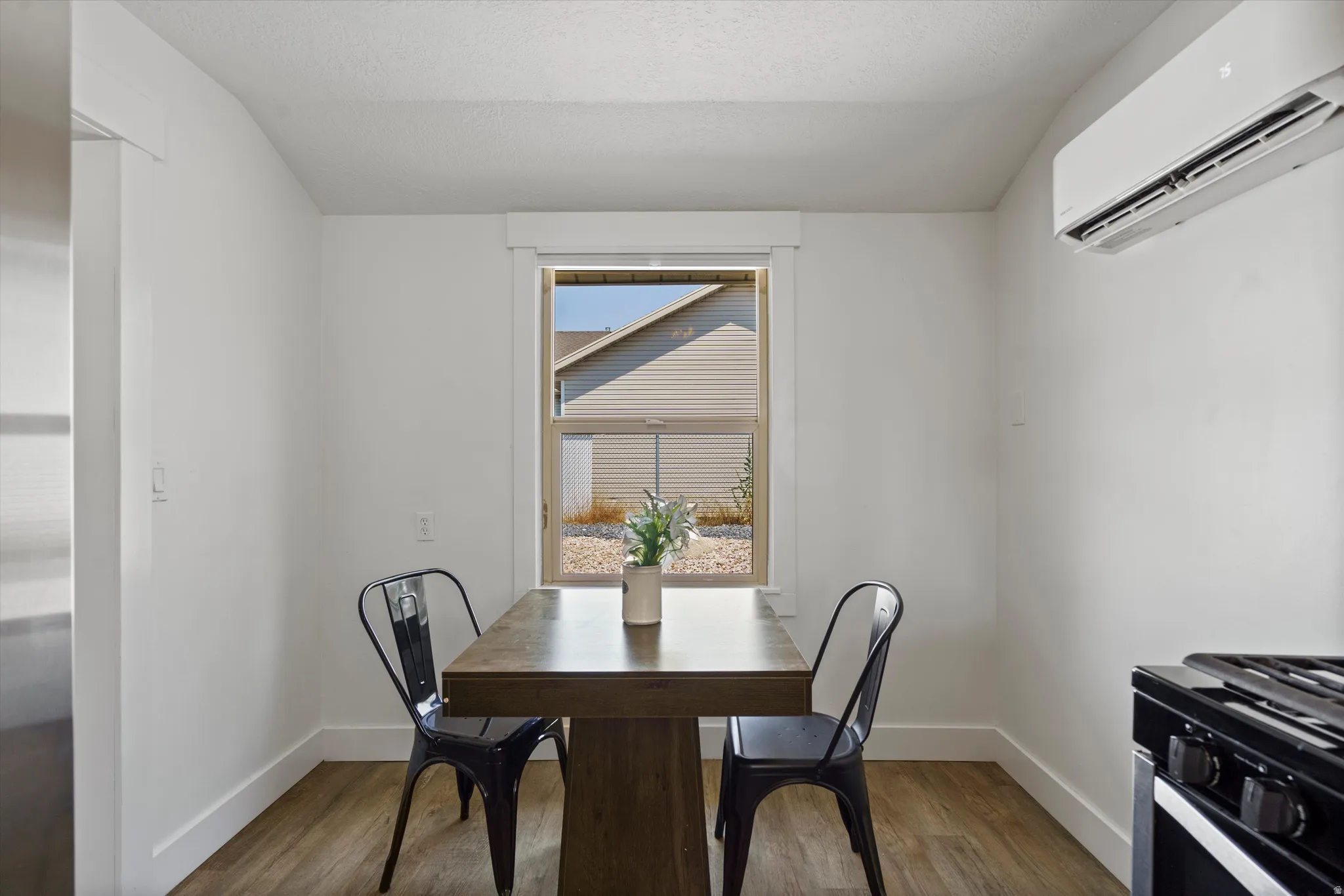 Compact dining area featuring a window with white trim, wood-finish flooring, and a wall-mounted air conditioning unit