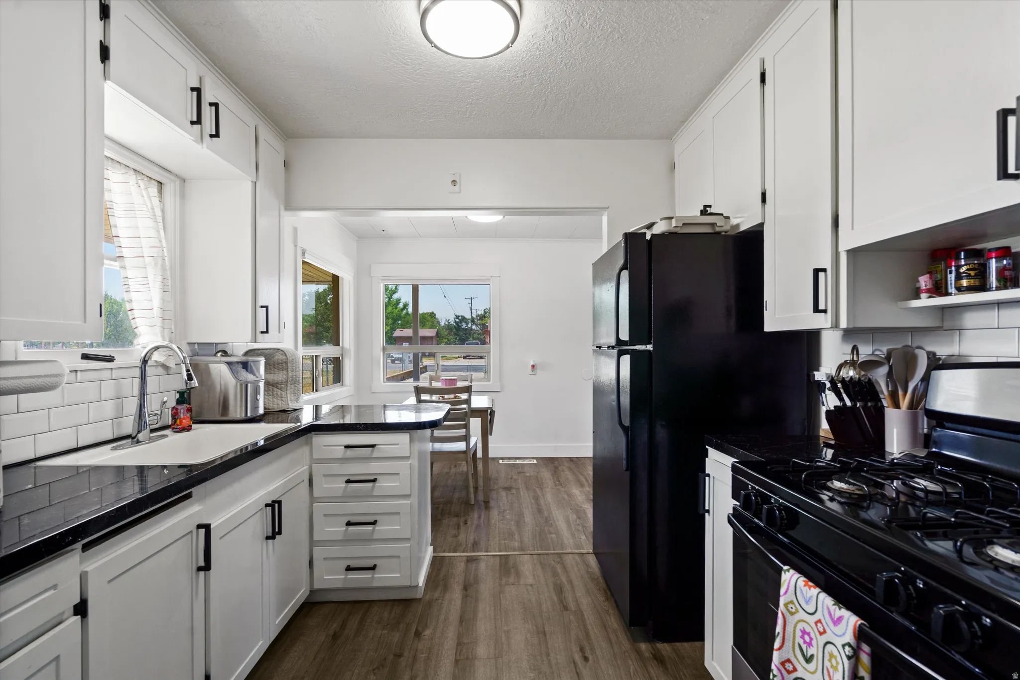 Galley kitchen featuring white cabinetry with matte black hardware, dark countertops, and a subway tile backsplash