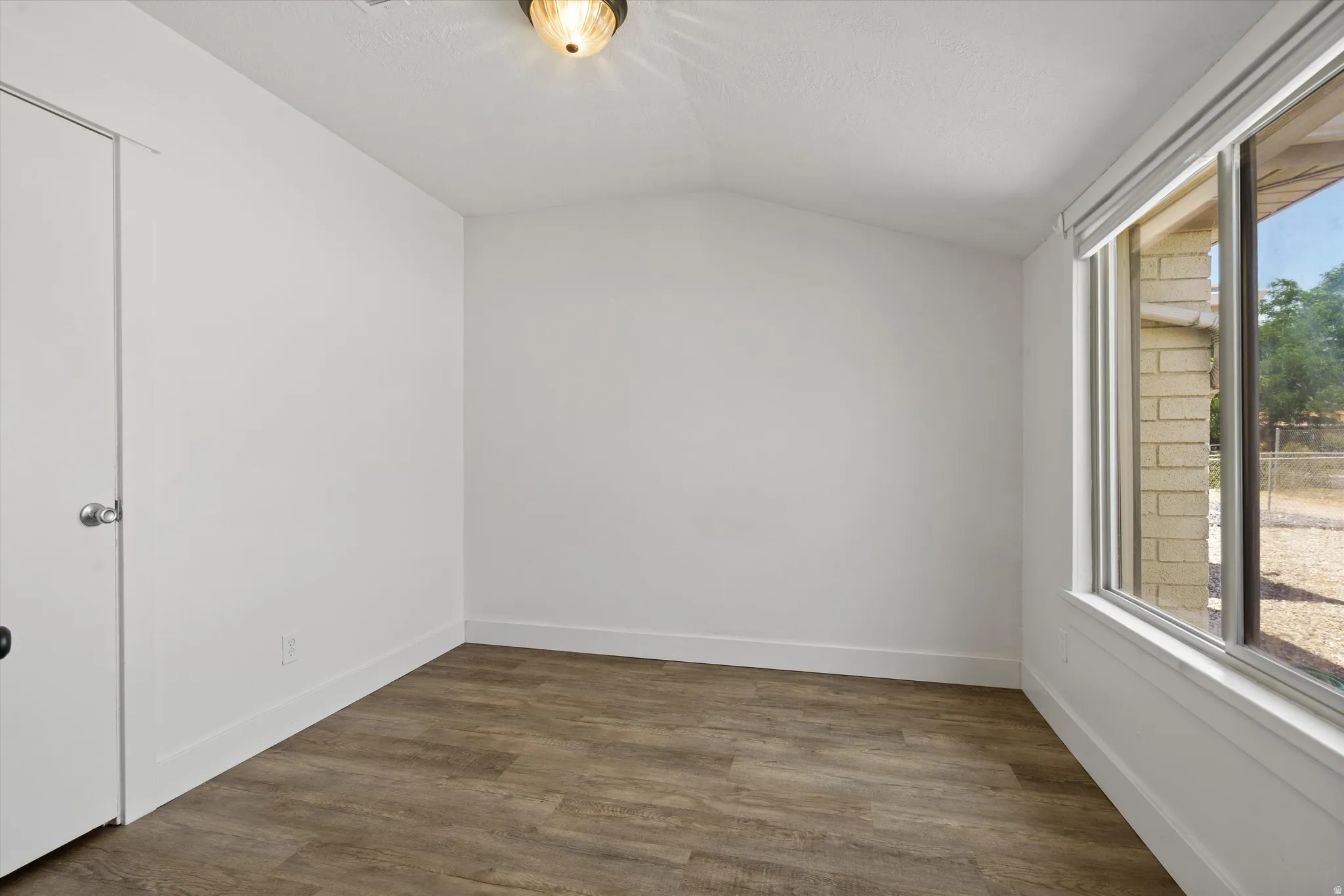 Room featuring wood-finish flooring, white walls, and a vaulted ceiling
