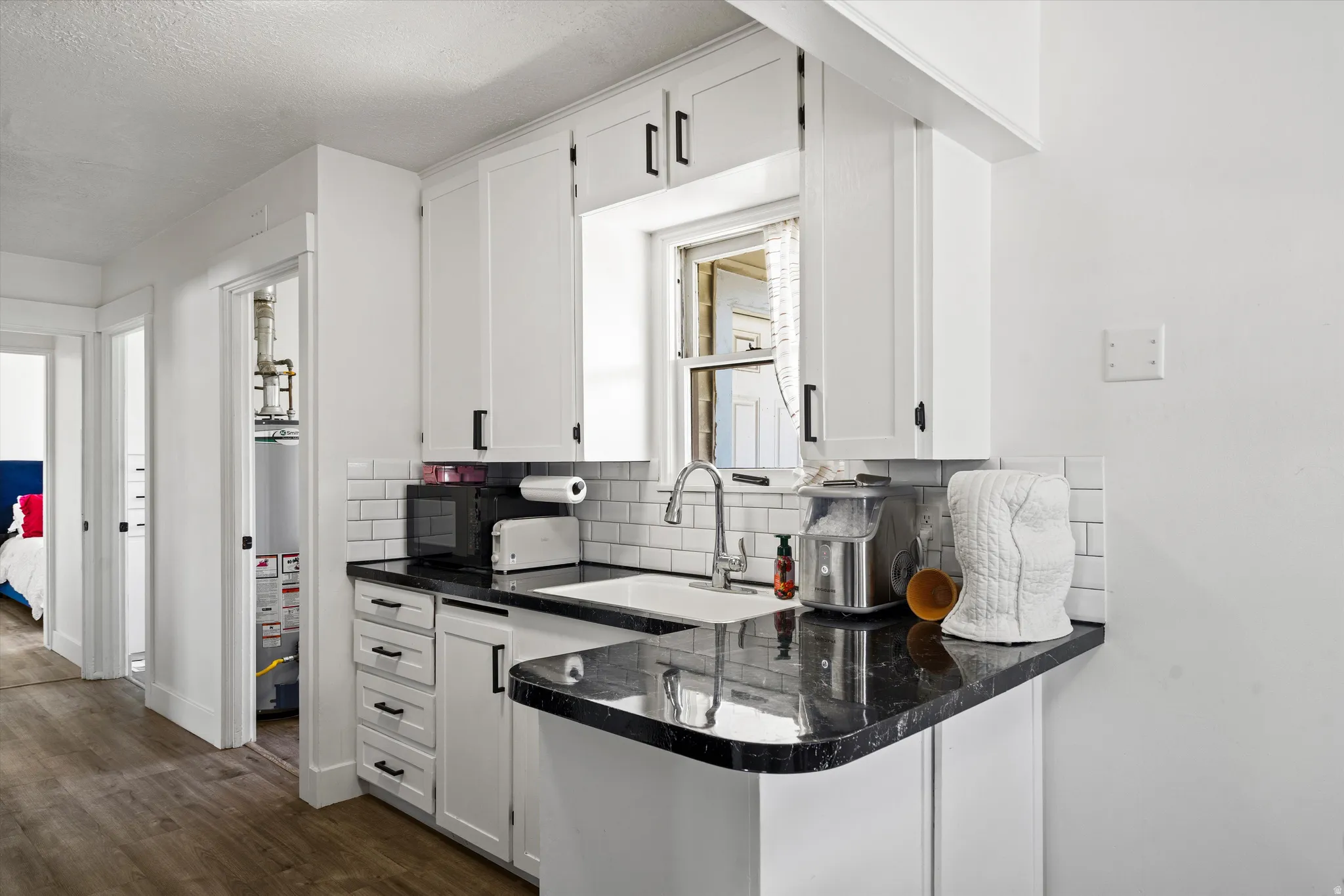 Kitchen featuring white cabinetry, dark countertops, a white subway tile backsplash, and a stainless steel faucet