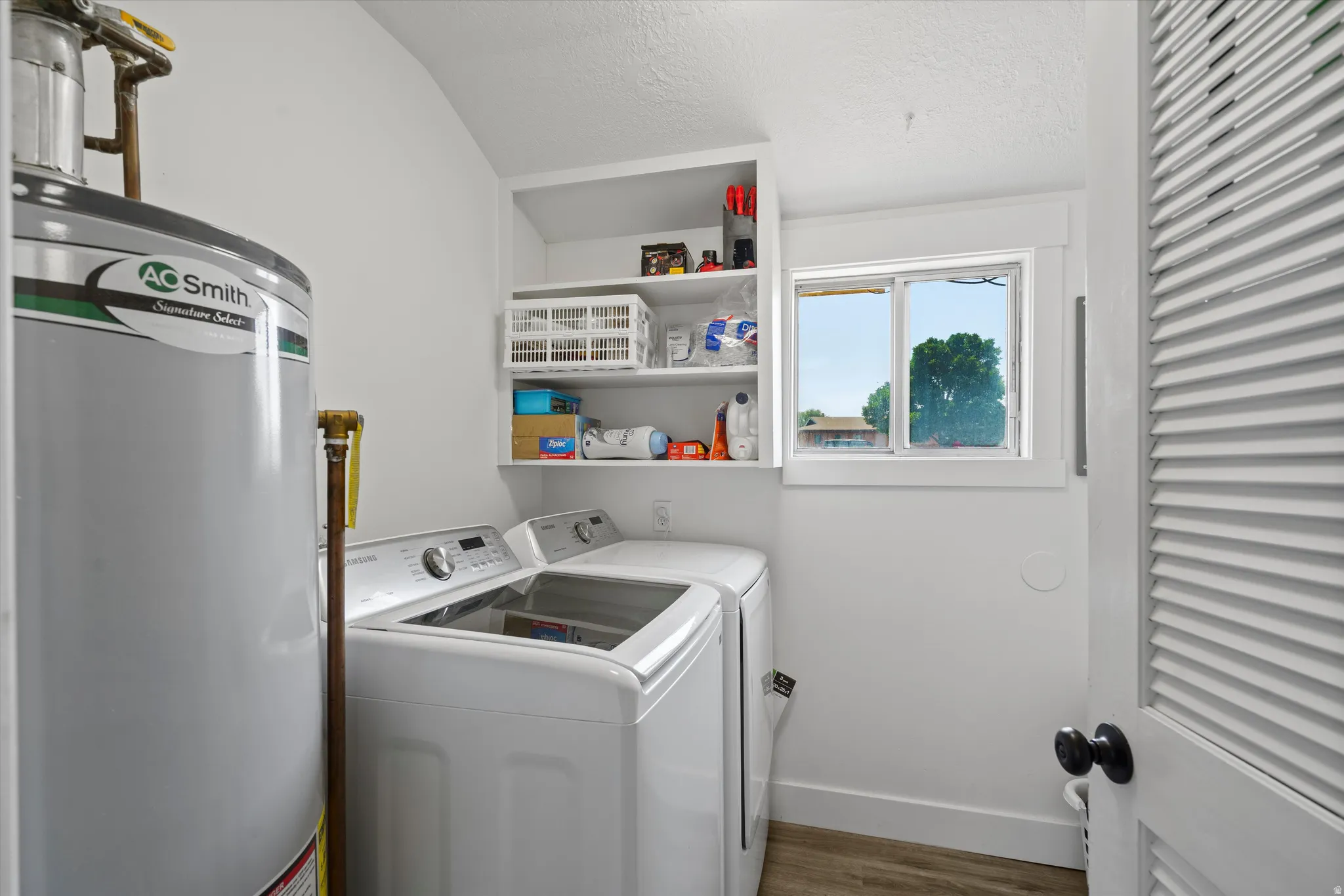 Dedicated utility area featuring a water heater, laundry appliances, a window, and built-in shelving