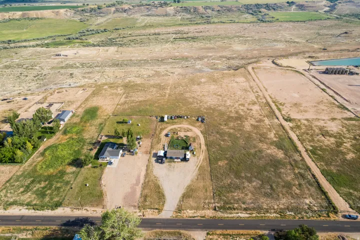 Expansive rural property featuring two residential structures with surrounding land, a paved road, and distant agricultural fields