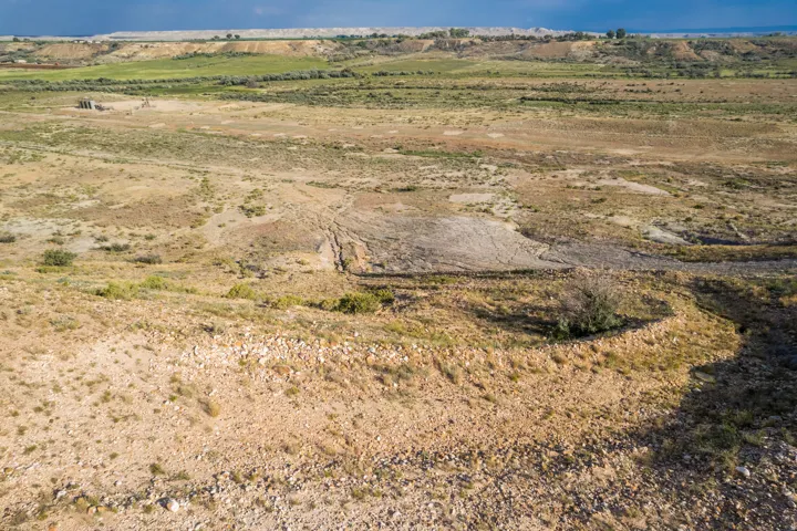 Expansive land offering diverse topography, including a large open field, rolling hills, and a distant green landscape