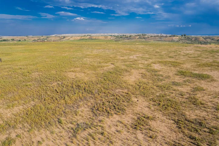 Expansive open land with natural ground cover, featuring distant low-lying hills and a broad sky overhead