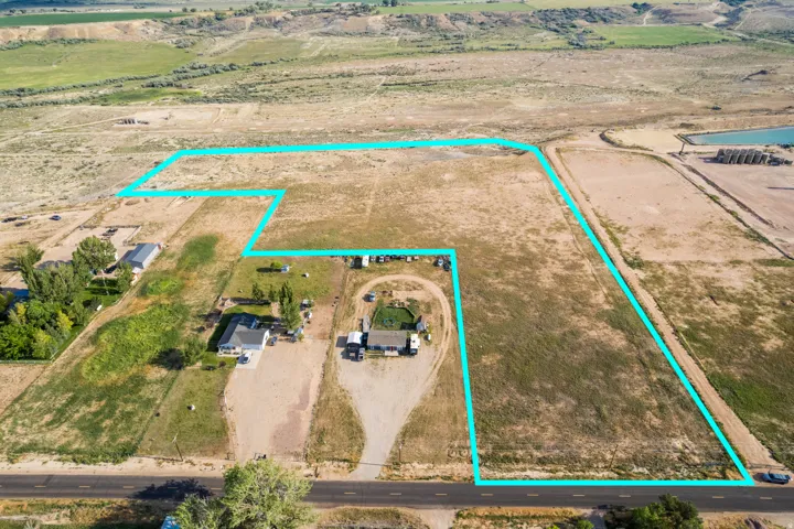 Expansive land parcel featuring existing structures, a paved road frontage, and varied terrain including open fields and distant hills