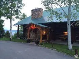 Log cabin exterior with a stone chimney, covered entryway, and a green corrugated metal roof