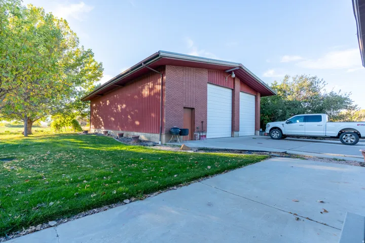 Detached structure featuring a red brick facade, two white overhead garage doors, a pedestrian entry door, and a concrete driveway