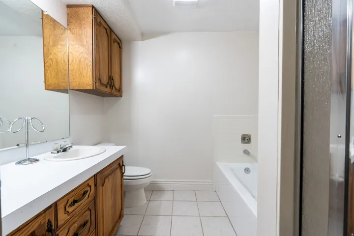 Bathroom featuring a built-in vanity with wood cabinetry and a white countertop, coordinating overhead wood cabinetry, a white toilet, and a white bathtub with tile surround