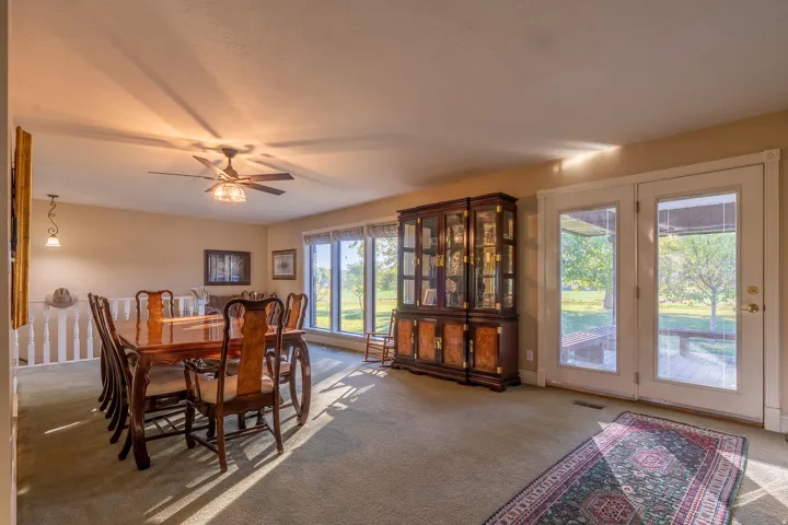 Carpeted interior space featuring a ceiling fan with integrated lighting, wall-mounted light fixture, and a white baluster railing