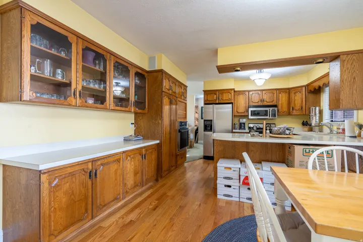 Expansive kitchen featuring wood-finish flooring, abundant wood cabinetry, integrated stainless steel appliances, and a breakfast bar with solid surface countertop