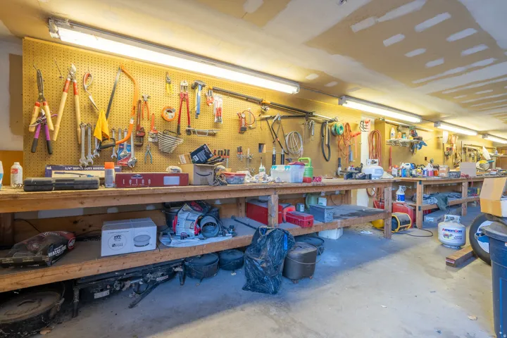 Dedicated workshop space featuring a full-length workbench, extensive pegboard organization, concrete flooring, and ample fluorescent lighting
