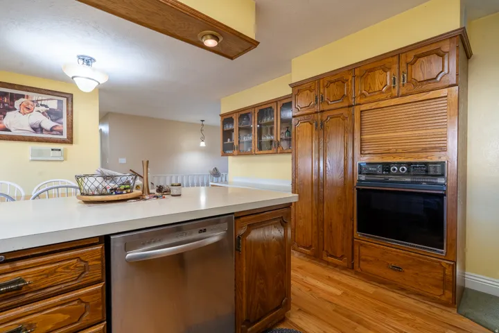 Kitchen featuring warm wood cabinetry, light-toned countertops, a built-in oven, and a stainless steel dishwasher