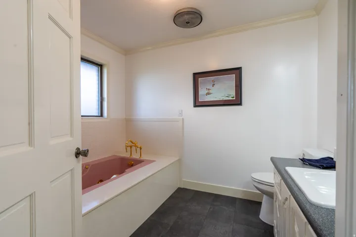 Bathroom featuring a built-in pink bathtub with brass fixtures, a vanity with a white basin and dark countertop, and dark-toned tile flooring