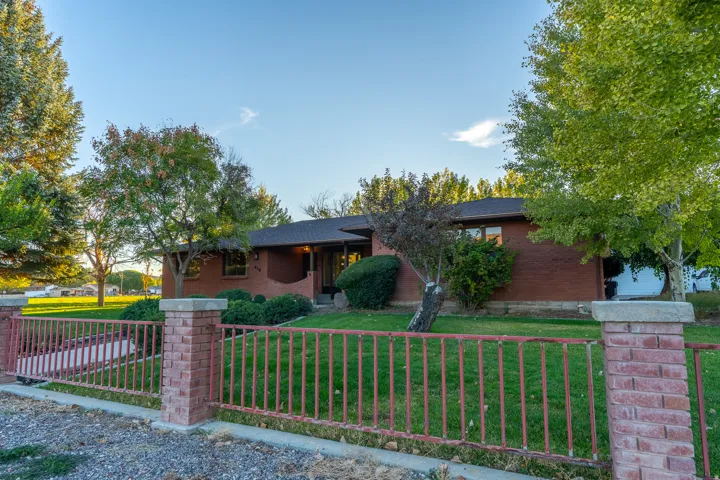 Brick ranch-style residence featuring a dark shingle roof, mature landscaping, and a front yard with established trees