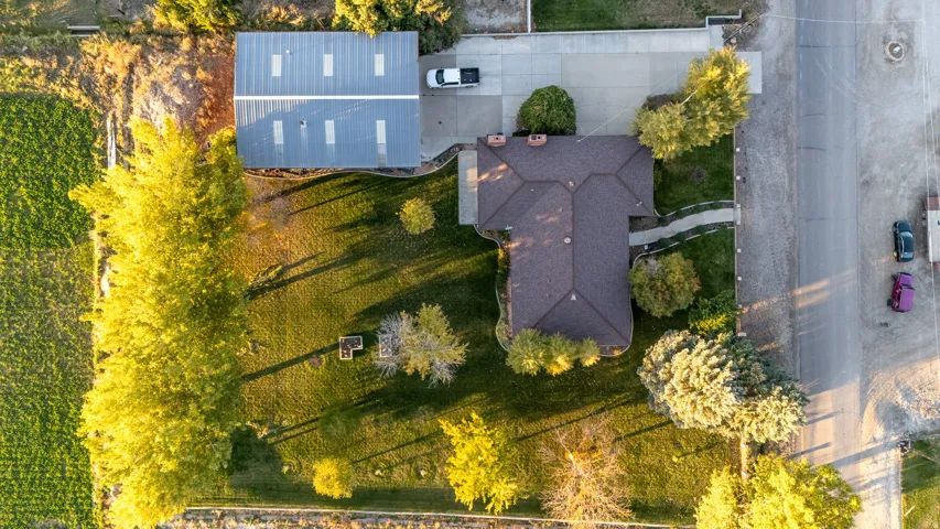 Aerial view showcasing a property with a brown shingle roof, established landscaping, a concrete driveway, and an extensive metal-roofed outbuilding with skylights
