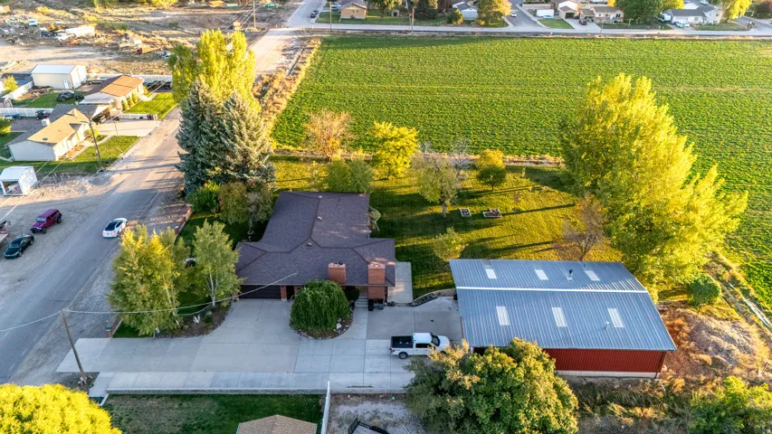 Property featuring a large red barn with a metal roof, a main residence with a dark shingle roof, mature trees, and a paved driveway