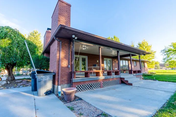 Brick exterior featuring a covered porch with decorative lattice, concrete patio, and mature trees