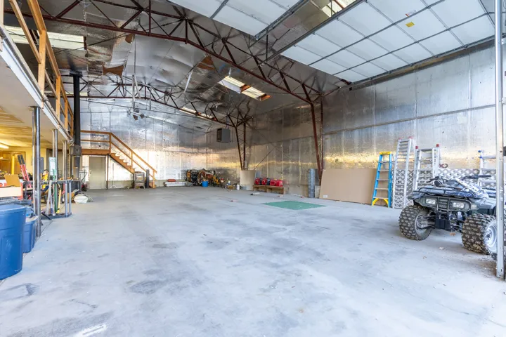 Spacious concrete-floor interior featuring a high ceiling, exposed structural beams, and a substantial overhead door