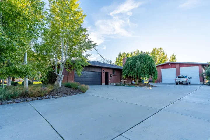 Expansive concrete driveway with a brick-clad residence featuring an attached garage and a detached multi-bay garage structure
