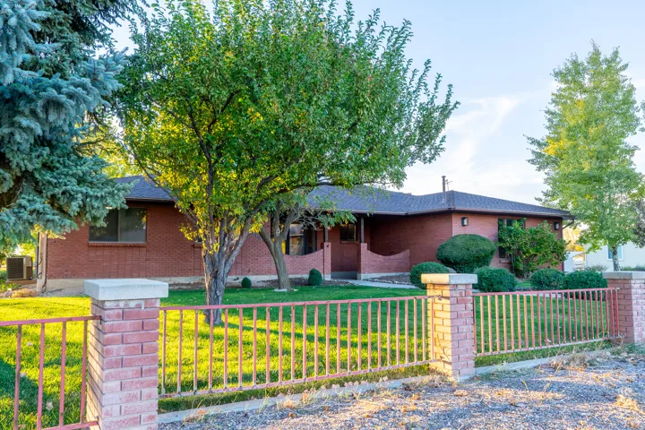 Brick exterior residence featuring a dark shingle roof, mature landscaping, and a front yard with established trees