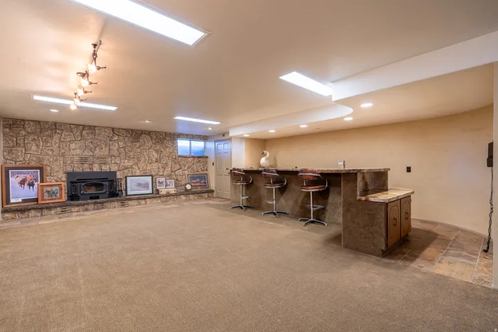 Spacious entertainment area featuring a stone accent wall with a built-in wood-burning fireplace, a built-in wet bar with a countertop, recessed lighting, and track lighting