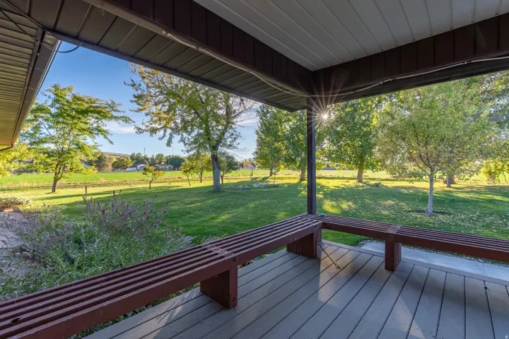Covered patio featuring wood-finish decking, built-in benches, and an expansive lawn beyond