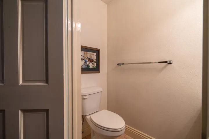 Compact water closet featuring a white toilet, light-colored walls, and a chrome towel bar