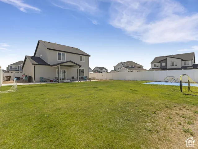 Expansive backyard featuring a manicured lawn, full vinyl privacy fencing, and a covered concrete patio