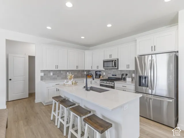 Contemporary kitchen featuring white cabinetry, stainless steel appliances, and a central island with a sink