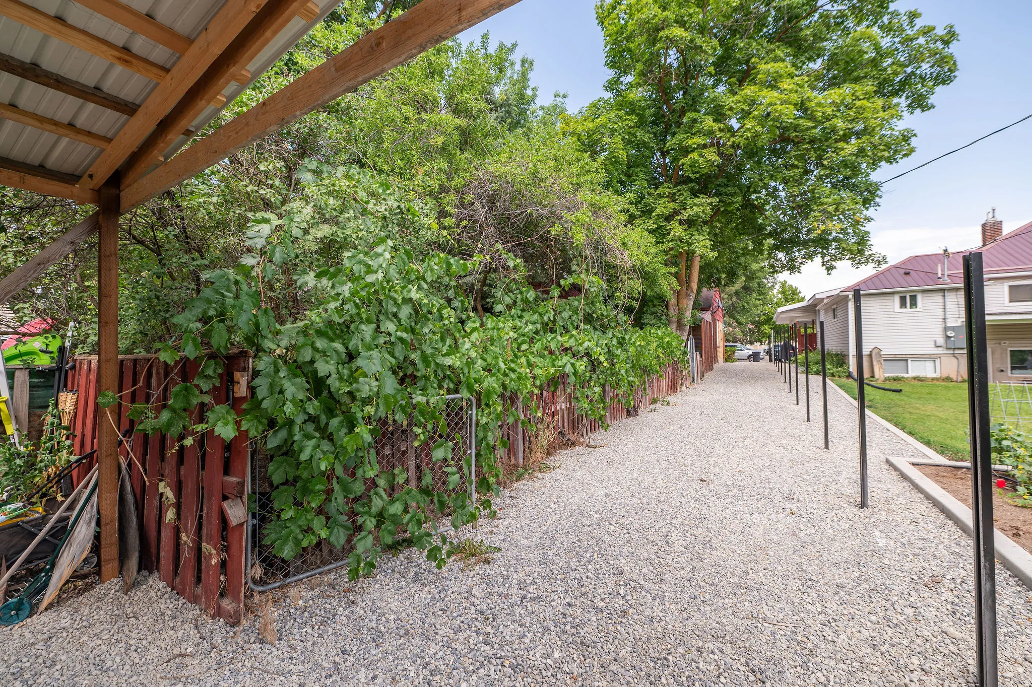 Gravel pathway bordered by a wooden fence with lush greenery and a covered structure