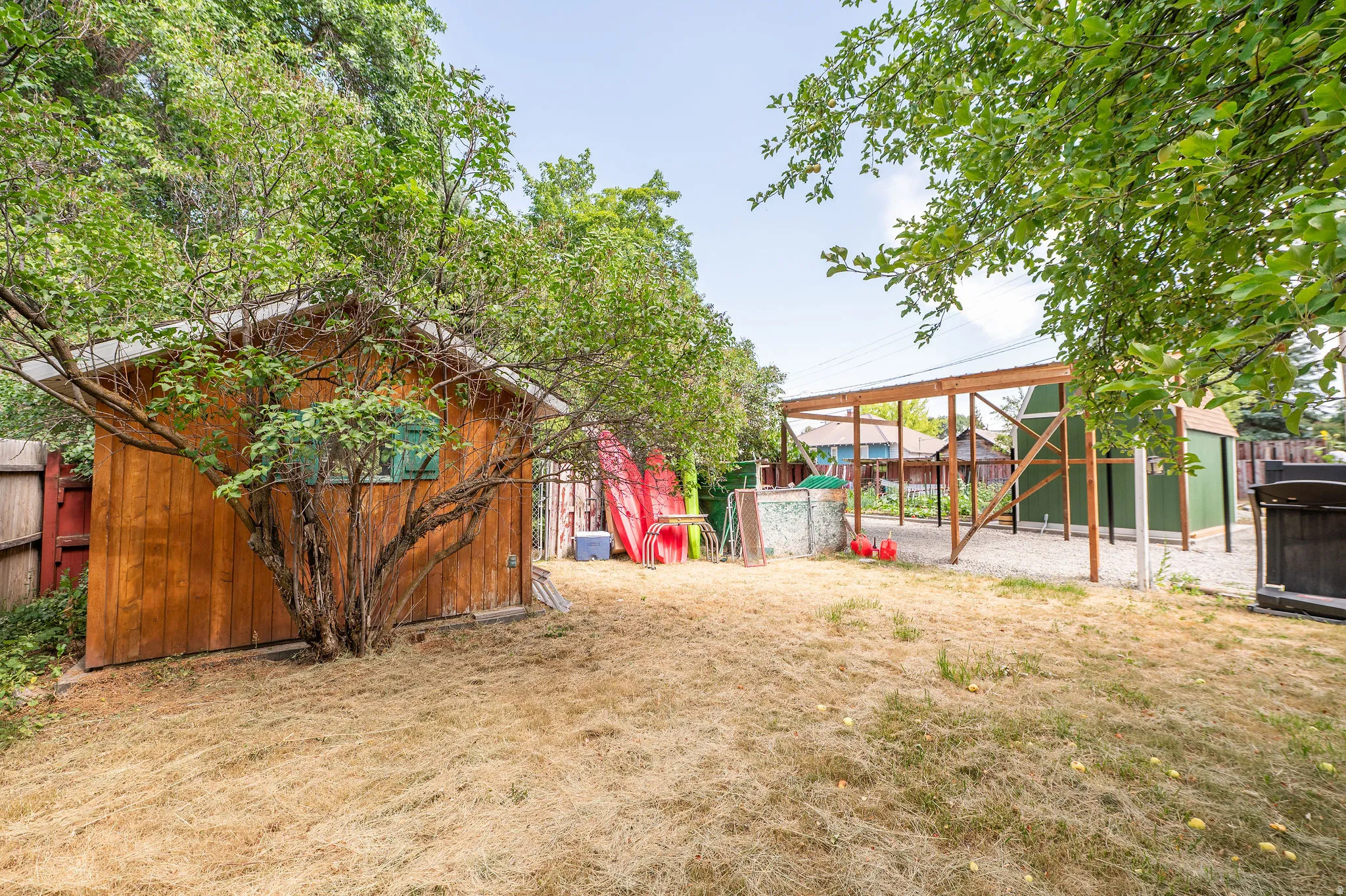 Expansive exterior featuring a wood-sided shed with a single window, mature trees, and a gravel-covered area with a large open-sided structure
