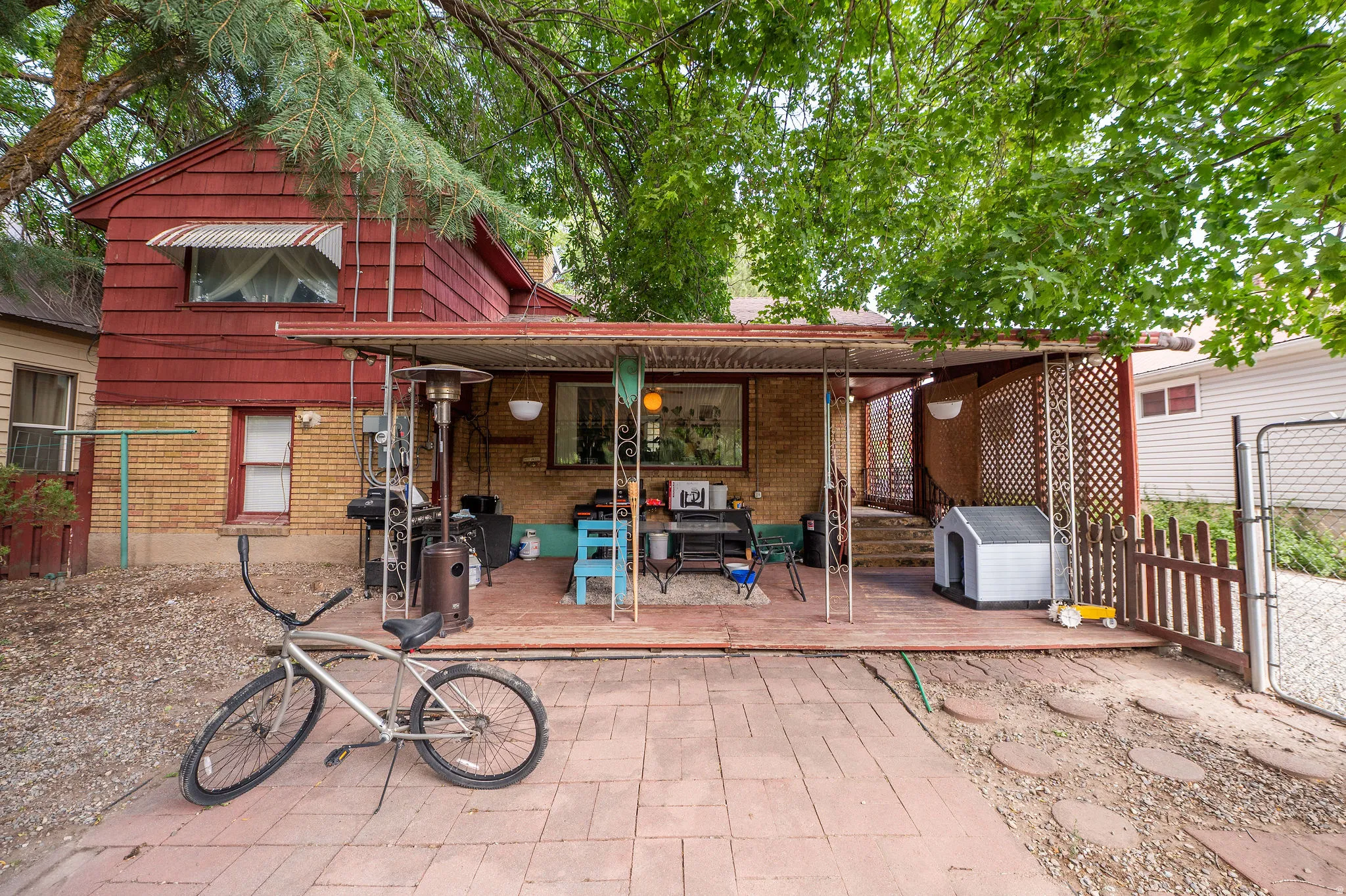 Rear exterior featuring a covered patio with lattice detailing, brick flooring, and a red shingle upper level