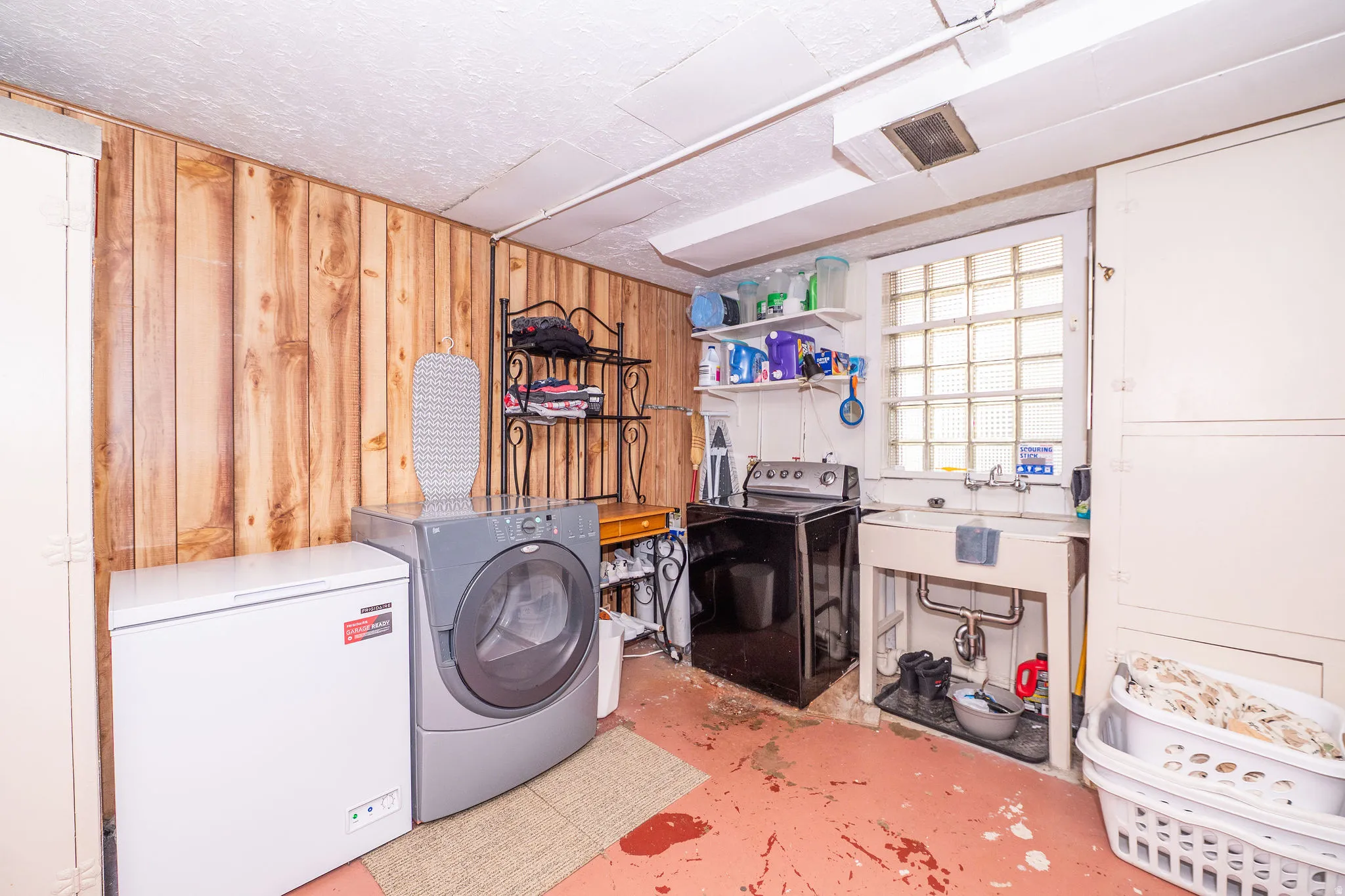 Functional utility space featuring wood paneling, a large utility sink, block glass window, and built-in storage cabinetry
