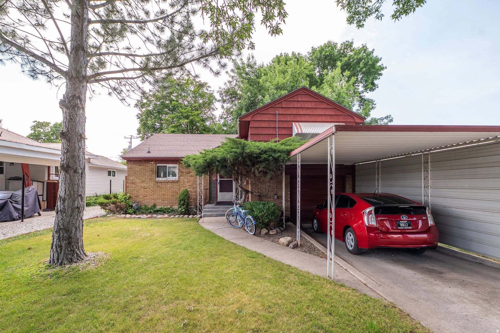 Brick exterior home featuring a covered carport, mature front yard tree, and front entry porch with steps