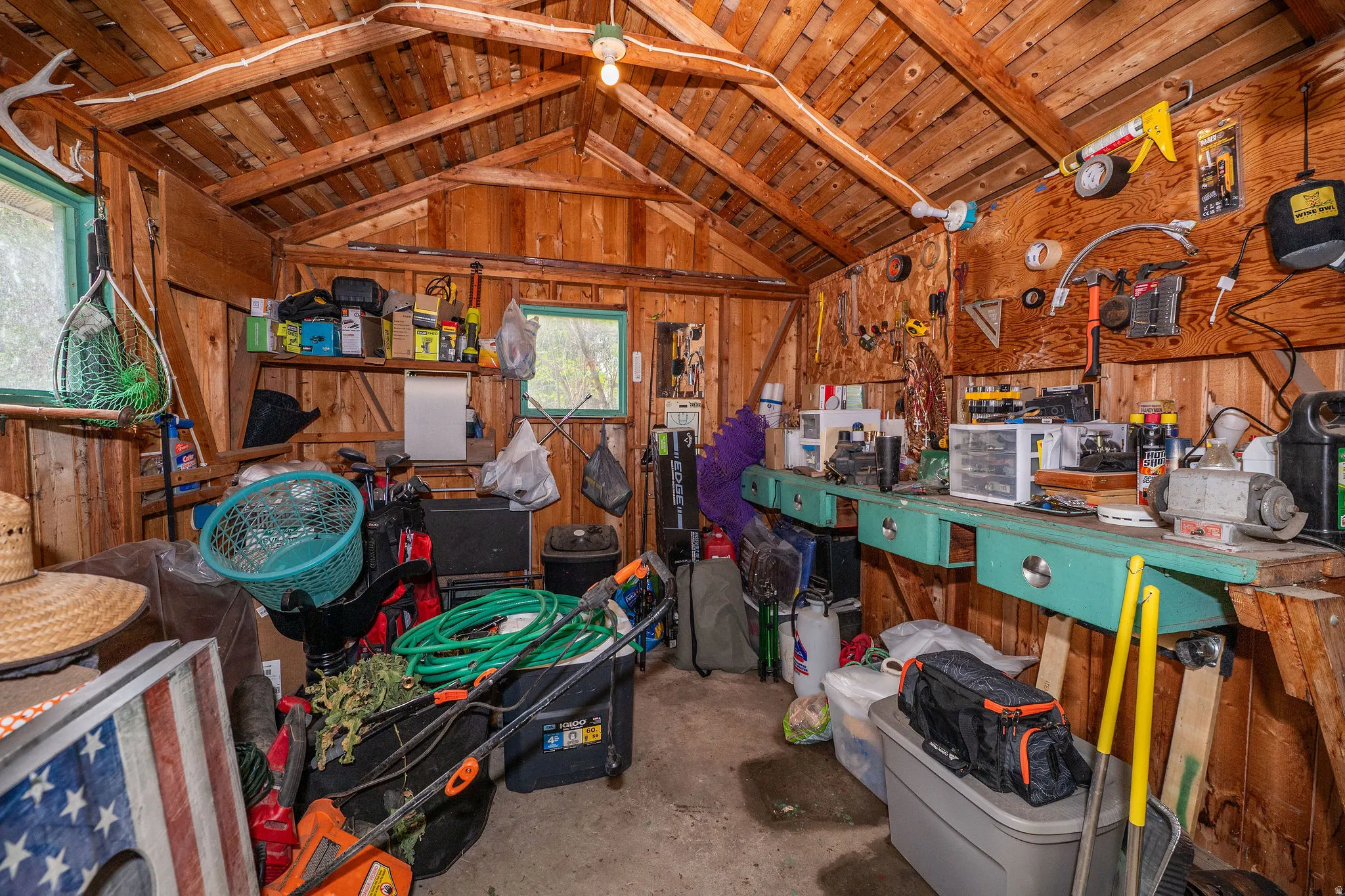 Utility structure featuring exposed wood plank walls and ceiling, a built-in workbench, two windows, and overhead lighting