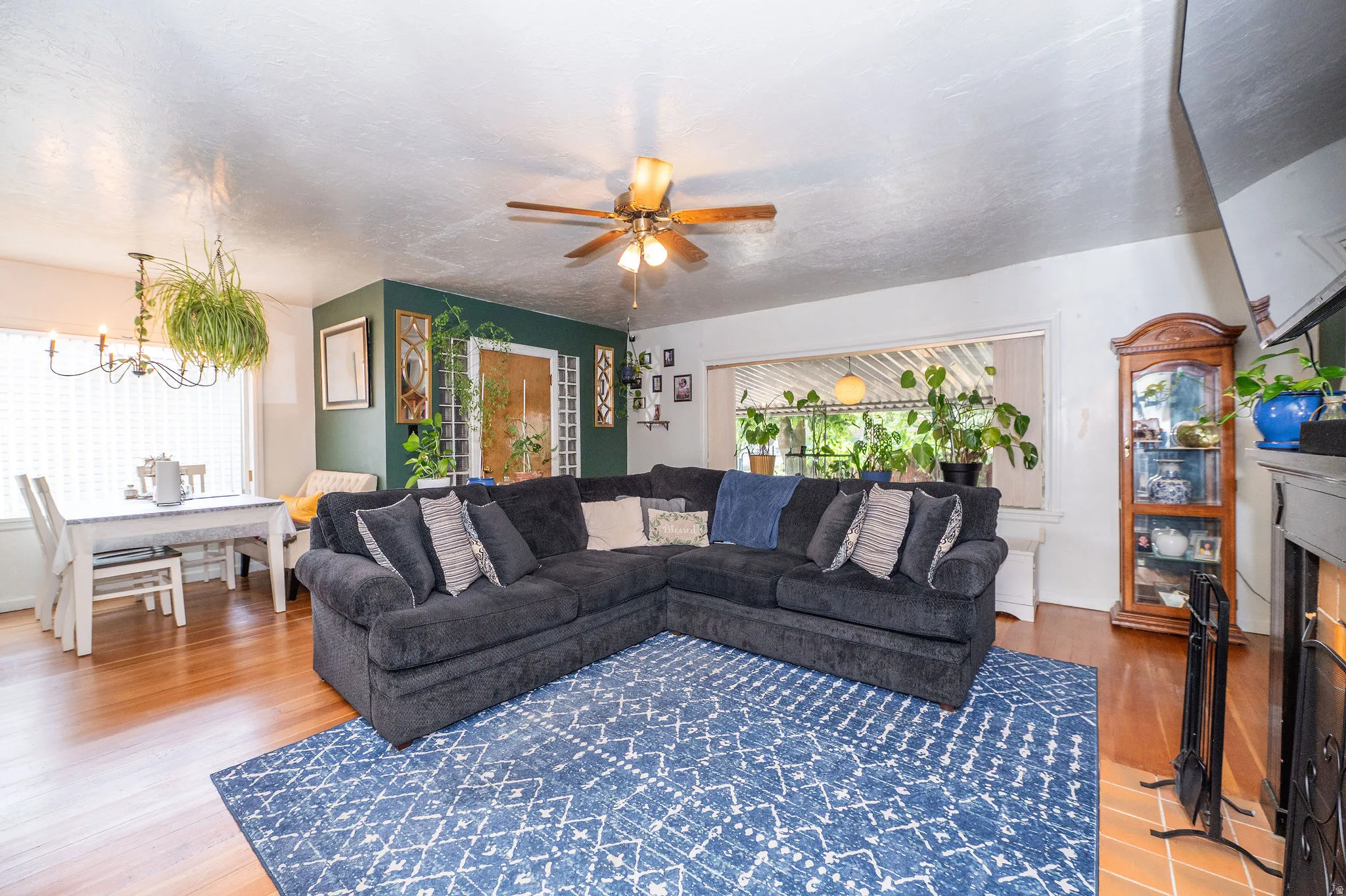 Open-concept living area featuring wood-finish flooring, a ceiling fan with integrated lighting, and a fireplace with a tile hearth